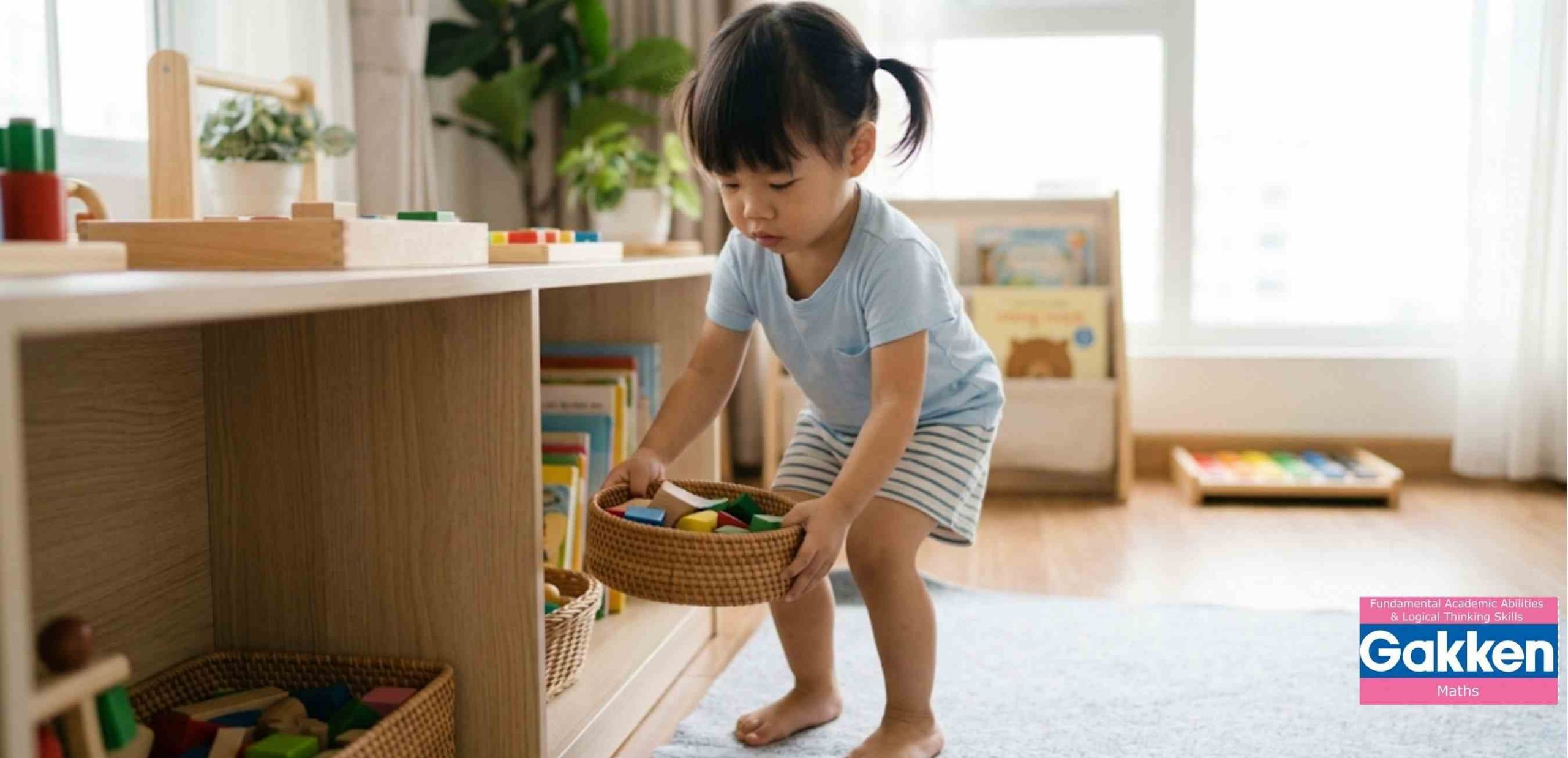 Bé tự cất các khối gỗ vào giỏ sau khi chơi, thể hiện tinh thần thay đổi giáo dục với trọng tâm phát triển Năng lực Tự lập và Quản trị bản thân, giúp trẻ hình thành tính tự giác, trách nhiệm và thói quen ngăn nắp từ sớm.